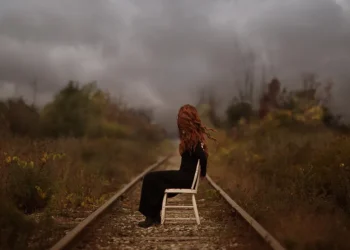 Patty Maher photography of a red-haired woman sitting on a chair on railway tracks