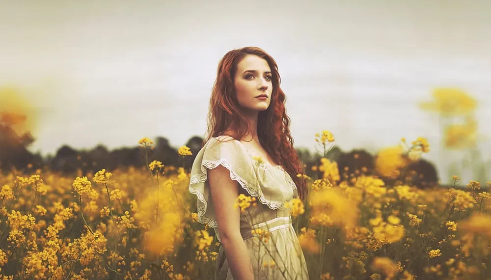 Red-haired woman in a white dress standing in a golden flower field