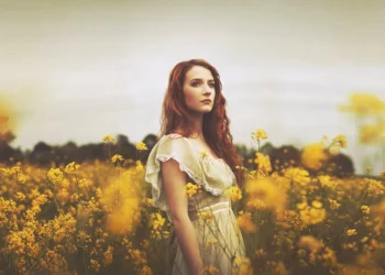 Red-haired woman in a white dress standing in a golden flower field