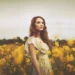 Red-haired woman in a white dress standing in a golden flower field