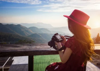 Woman in red hat holding a camera overlooking a mountain landscape at sunset