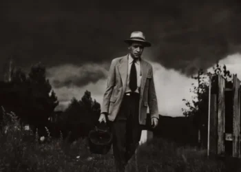 A weathered doctor walks through a field carrying a medical bag, stormy sky above