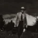 A weathered doctor walks through a field carrying a medical bag, stormy sky above