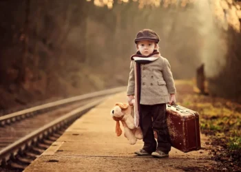 Children portrait photography: boy with teddy bear and suitcase at a railway platform