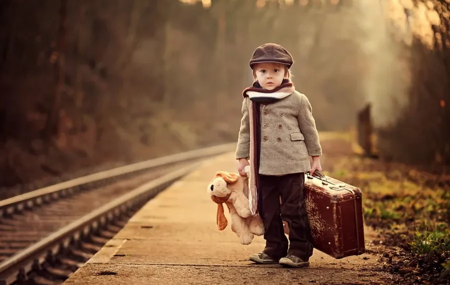 Children portrait photography: boy with teddy bear and suitcase at a railway platform