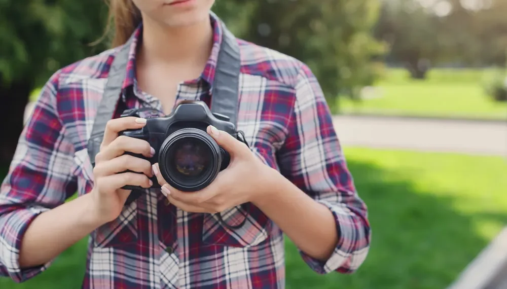 Young woman holding DSLR camera outdoors in a park