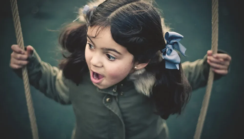 Little girl on a swing with a surprised expression outdoors