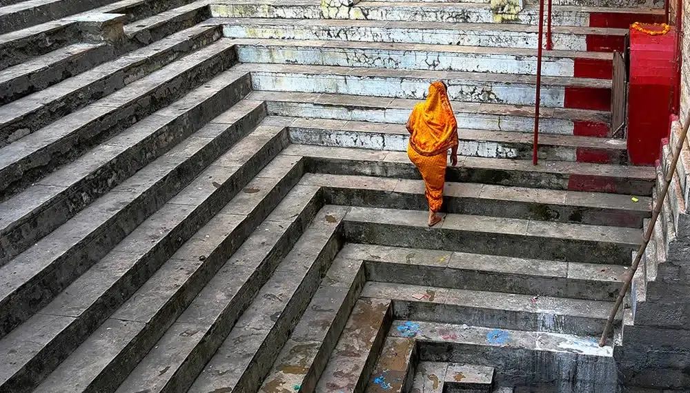 Woman in orange sari ascending ancient stone steps at a Varanasi ghat