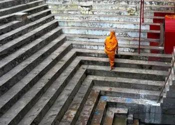 Woman in orange sari ascending ancient stone steps at a Varanasi ghat