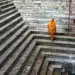 Woman in orange sari ascending ancient stone steps at a Varanasi ghat