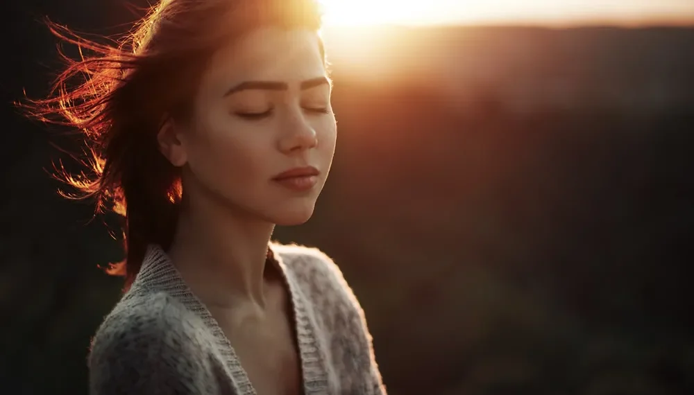 Woman with closed eyes in warm sunset light outdoors
