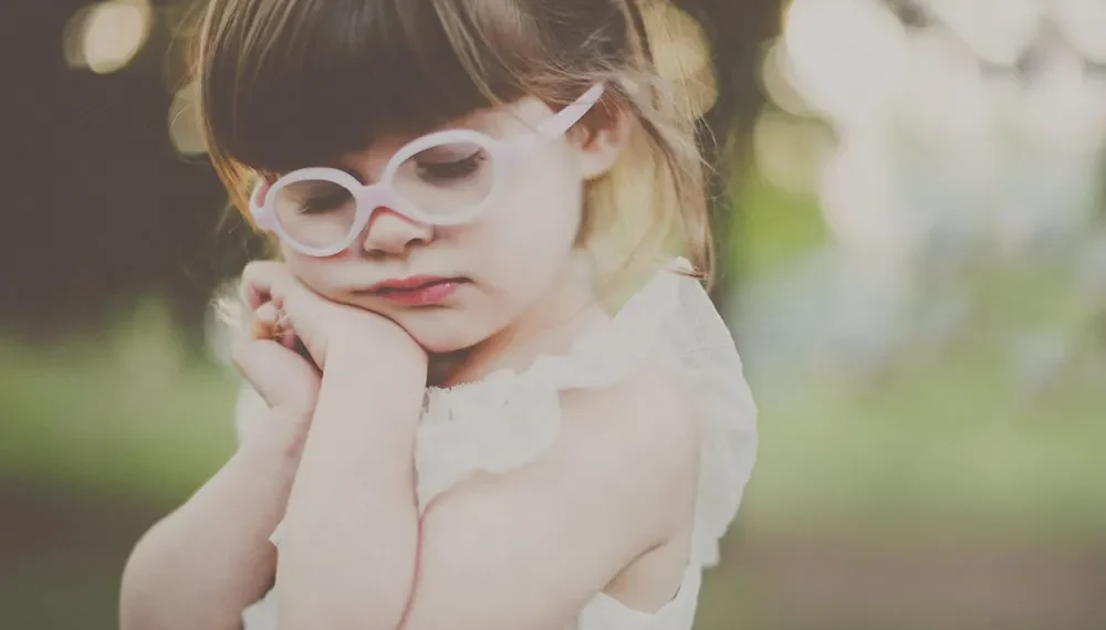 Little girl with pink glasses resting her head in soft natural light
