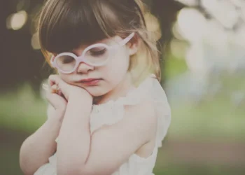 Little girl with pink glasses resting her head in soft natural light