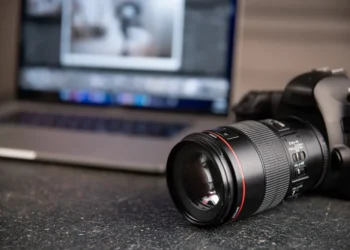 Canon DSLR camera and lens on a desk with a laptop showing photo editing
