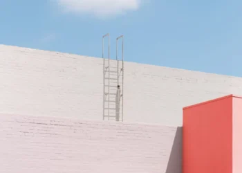 Ladder against a white wall beside a pink building under a blue sky