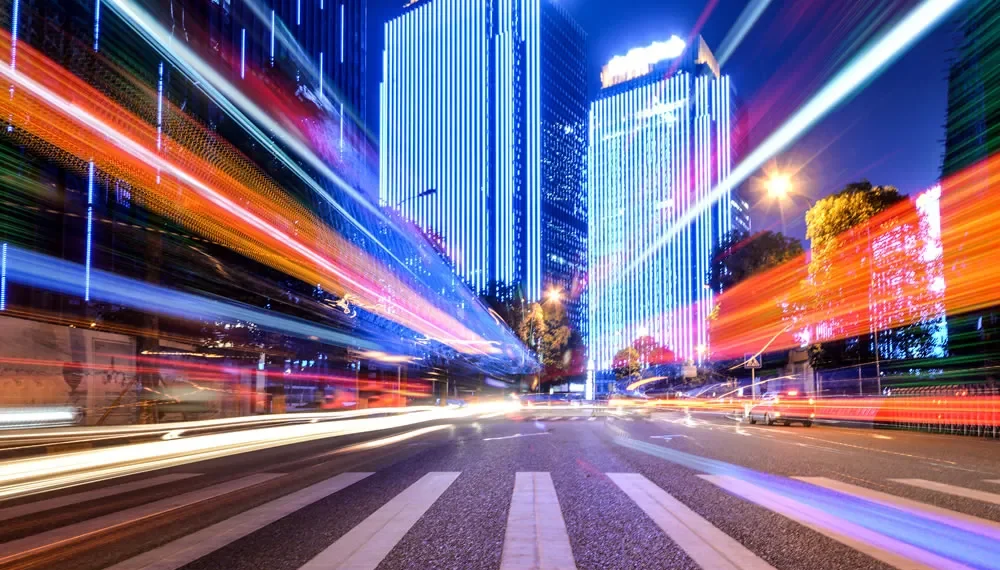 Long-exposure city street at night with colorful light trails and lit skyscrapers