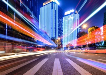 Long-exposure city street at night with colorful light trails and lit skyscrapers
