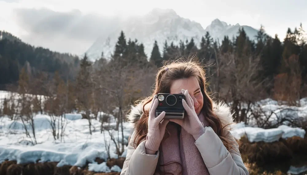 Woman using a Polaroid camera outdoors in a snowy mountain landscape