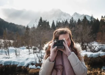 Woman using a Polaroid camera outdoors in a snowy mountain landscape