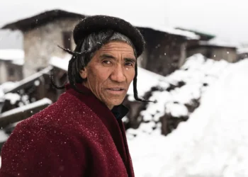 Brokpa man in traditional hat and red coat standing in a snowy Bhutan village