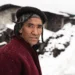 Brokpa man in traditional hat and red coat standing in a snowy Bhutan village
