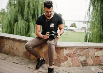 Male photographer sitting on a stone wall reviewing shots on his DSLR camera