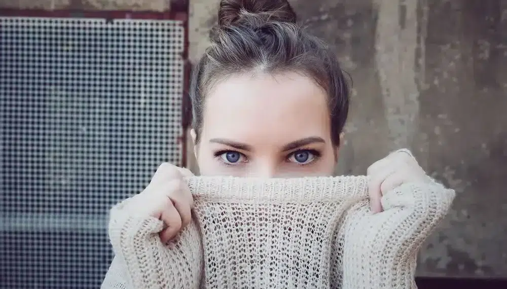 Portrait of woman with blue eyes hiding face behind knitted sweater