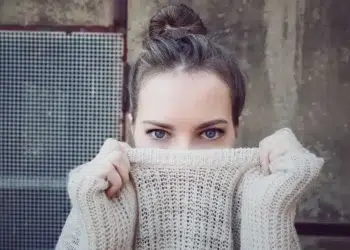 Portrait of woman with blue eyes hiding face behind knitted sweater