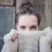 Portrait of woman with blue eyes hiding face behind knitted sweater