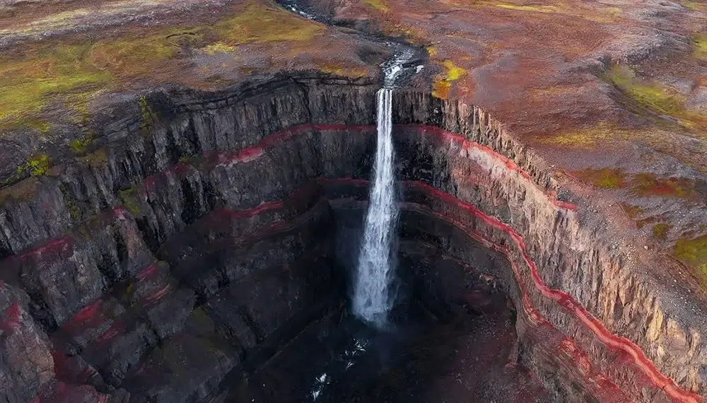 Aerial view of a waterfall plunging into a red-layered canyon