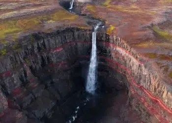 Aerial view of a waterfall plunging into a red-layered canyon