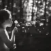 A child blowing dandelion seeds in a forest, black and white