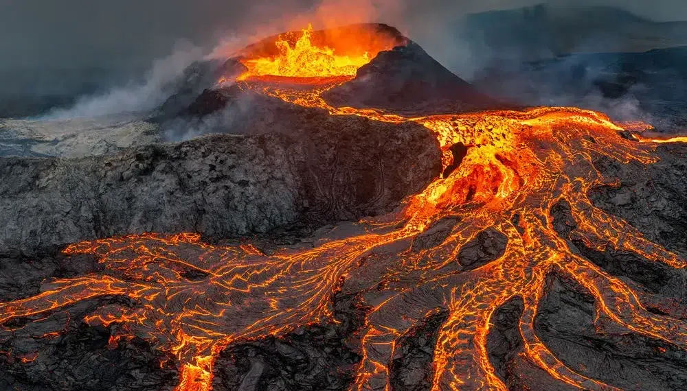 Glowing lava flows streaming down an erupting volcano