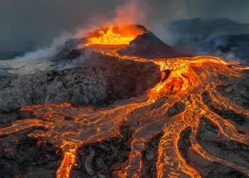 Glowing lava flows streaming down an erupting volcano