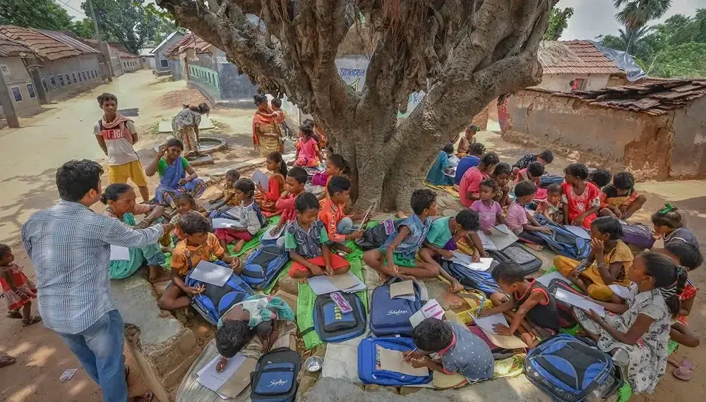 Teacher conducting an outdoor class for children under a large tree in rural India