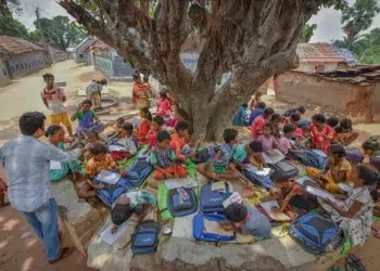 Teacher conducting an outdoor class for children under a large tree in rural India
