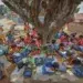 Teacher conducting an outdoor class for children under a large tree in rural India