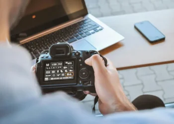 Person holding a DSLR camera showing manual settings screen at a desk