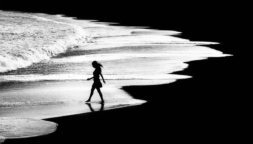 Woman silhouette walking along shoreline, black and white artistic photography