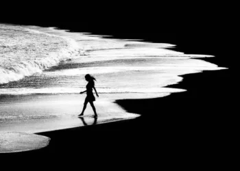 Woman silhouette walking along shoreline, black and white artistic photography