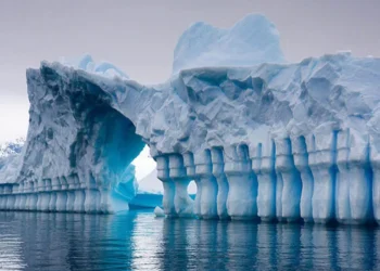 Iceberg with natural arch and blue ice reflections over calm ocean water