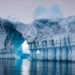 Iceberg with natural arch and blue ice reflections over calm ocean water