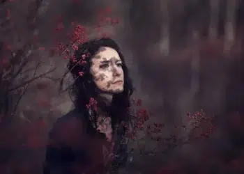 Moody portrait of a woman surrounded by red berries with dappled shadow on her face