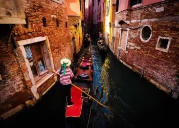 Gondolier steering through a narrow Venice canal lined with brick buildings