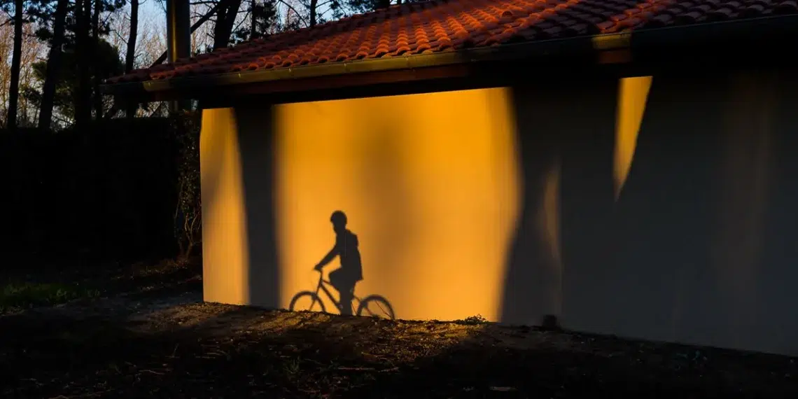 Cyclist shadow cast on sunlit wall beside tiled-roof building