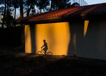 Cyclist shadow cast on sunlit wall beside tiled-roof building