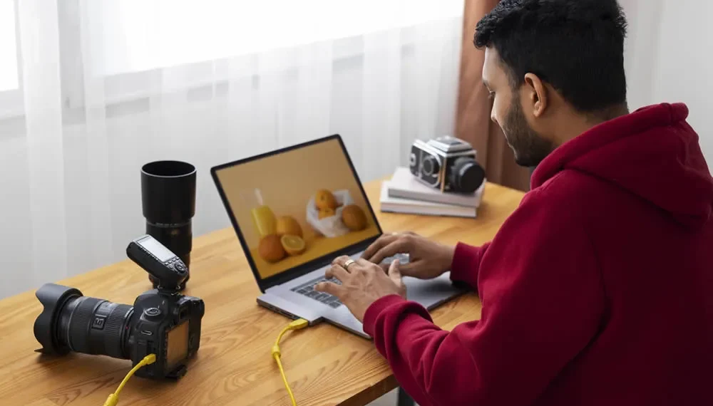 Photographer editing a food photo on a laptop with cameras and lenses nearby