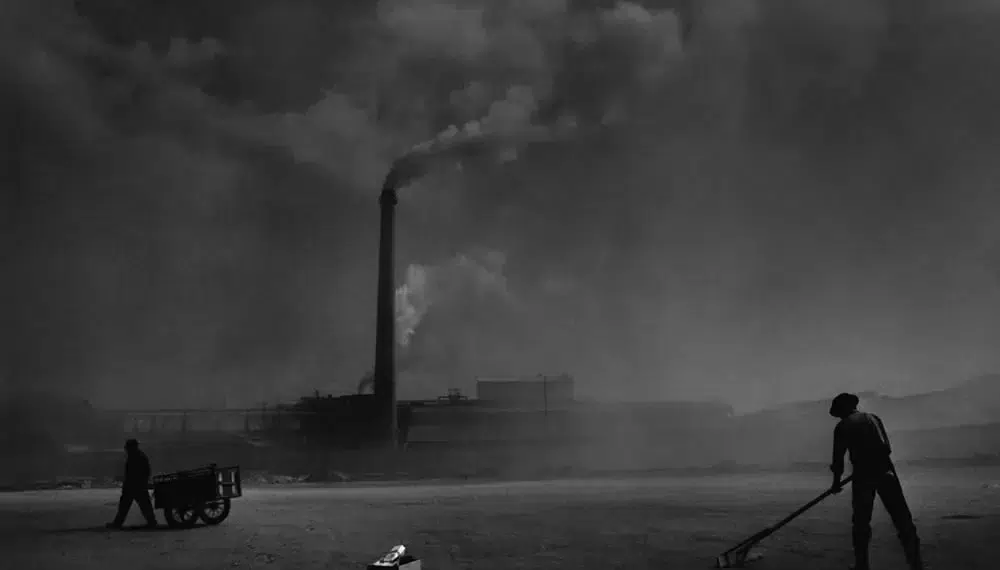 Iconic Visions: 30 Powerful Monochrome Photos by Renowned Photographers 31 Workers toiling near a smoky factory chimney in a dark b&w industrial scene
