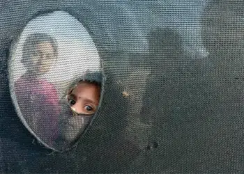 Child peeking through a hole in a dark mesh net with curious eyes