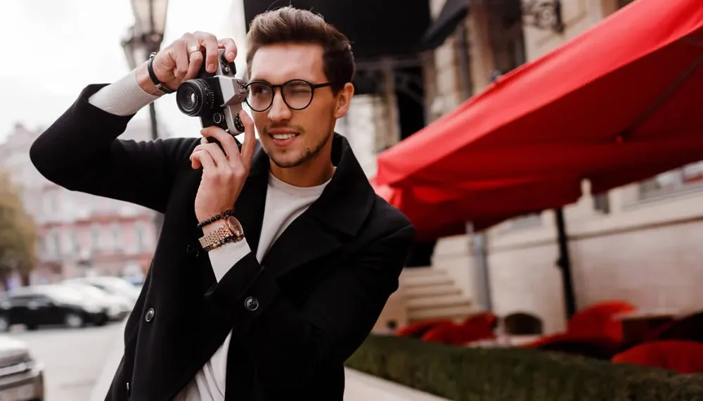 Stylish man with glasses taking photos on a film camera outdoors